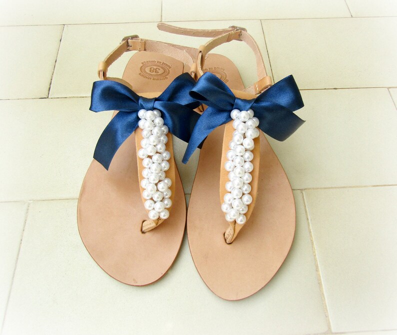 May include: A pair of tan leather sandals with navy blue bows and pearl embellishments.