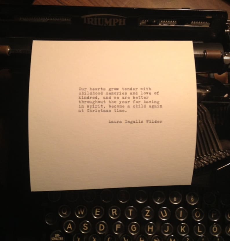 May include: A black and white image of a typewriter with a piece of paper inserted. The paper has a quote from Laura Ingalls Wilder that reads: "Our hearts grow tender with childhood memories and love of kindred, and we are better throughout the year for having in spirit, become a child again at Christmas time."