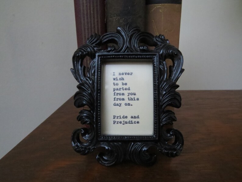 May include: A black ornate picture frame with a white background and a quote from Pride and Prejudice: "I never wish to be parted from you from this day on."