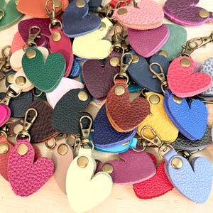 May include: A collection of heart-shaped keychains in various colors, including pink, blue, green, yellow, and brown. Each keychain features a textured surface, a brass-toned metal snap button, and a matching swivel lobster clasp for attachment.