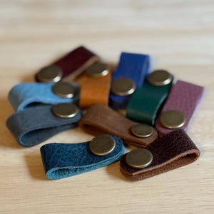 May include: A white ceramic mug with a black handle and the text "But First, Coffee" in a black, handwritten-style font. The mug is on a white surface.