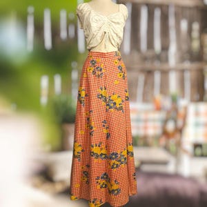 May include: A vintage two-piece outfit featuring a cream-colored crop top and a long, high-waisted skirt. The skirt has a red and white gingham pattern with yellow and blue floral accents. The outfit is displayed on a mannequin.