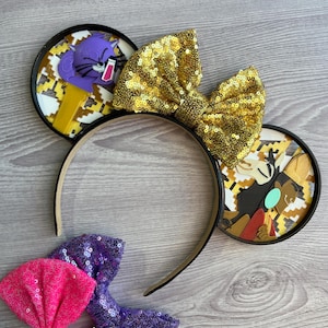 May include: Black mouse ears headband with a gold sequin bow. The ears feature a cartoon image of a cat and a dog with a patterned background.