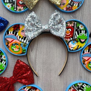 May include: A collection of headbands with sequined bow accents in gold, silver, and red. The headbands feature character-themed circular designs with a blue border. The background is a light wood grain.