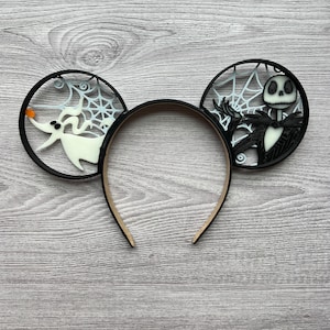 May include: Black and white mouse ears headband featuring a cutout of Jack Skellington from The Nightmare Before Christmas on one ear and a cutout of Zero, Jack's ghost dog, on the other ear.