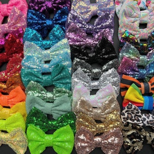 May include: A collection of sequined hair bows in various colors, including pink, blue, green, and gold. The bows are arranged closely together, showcasing their sparkly texture and diverse hues. The bows are a mix of solid colors and patterned designs.