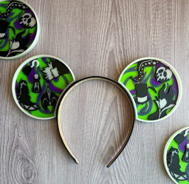 May include: Black headband with mouse ears featuring a green, purple, and black design. The ears have a white border and depict various villainous characters and symbols, including skulls, tentacles, and silhouettes.