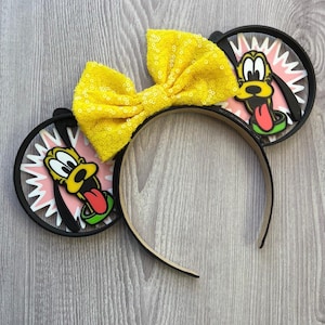 May include: A headband featuring black mouse ears with Pluto character designs. The ears have a pink and white burst design. A large yellow sequined bow sits between the ears. The headband is black and tan.