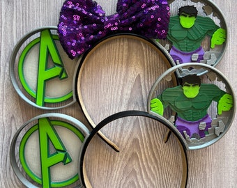 May include: A pair of gray mouse ears with a purple sequined bow. One ear features a green and gray Avengers logo, the other ear features a green Hulk character.