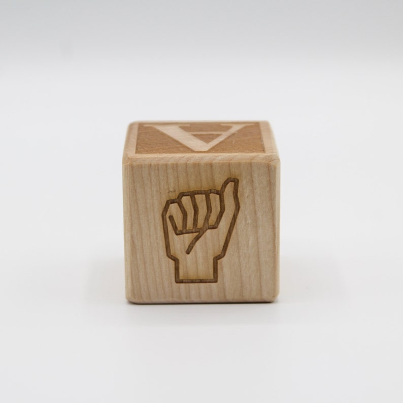 May include: Wooden block with the letter "V" and a sign language hand gesture for the letter "V" on the front.