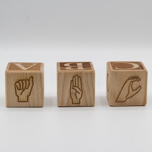 May include: Three wooden blocks with the letters A, B, and C, each with a different sign language hand gesture.