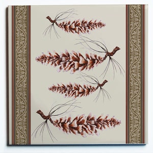 May include: A square decorative tile featuring four detailed illustrations of pine cones in shades of brown and white against a cream background. The tile has a decorative border with floral and geometric patterns in brown and beige.