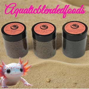 May include: Three clear jars with black lids, labeled "Mini Bloodworm Sticks," "Mini Bug Sticks," and "Mini Blackworm Pellets." The jars sit on sand next to a cartoon axolotl. The text "Aquaticblendedfoods" is above the jars.