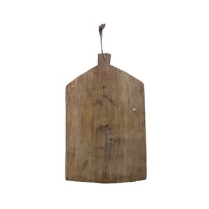 May include: A rustic wooden cutting board with a slightly rounded shape and a rope handle. The board has a natural wood grain and shows signs of wear and use.