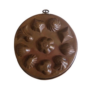 May include: Antique copper cake mold with 12 different shaped cavities for baking small cakes or pastries. The mold has a handle on top.