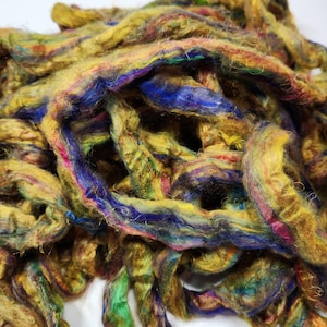 May include: A pile of colorful, hand-spun yarn in shades of gold, blue, green, and purple. The yarn is made from natural fibers and has a soft, fluffy texture.