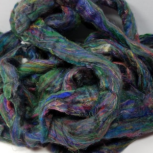 May include: A close-up of a bundle of colorful, hand-spun yarn. The yarn is a mix of dark blue, green, and purple shades with hints of red and yellow. The yarn is soft and fluffy, and it would be perfect for knitting or crocheting.