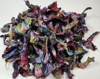May include: A pile of colorful, hand-dyed silk ribbon scraps. The ribbon is a mix of purple, blue, green, and yellow colors. The ribbon is perfect for crafting and art projects.