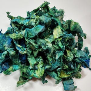 May include: A pile of teal, green, and blue silk fabric scraps. The fabric is hand-dyed and has a textured, crinkled look.