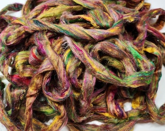 May include: A pile of colorful, hand-spun silk fiber in shades of gold, green, pink, and purple. The fiber is soft and fluffy, and it would be perfect for spinning, felting, or weaving.