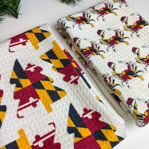 May include: Two white kitchen towels with Maryland-themed designs. One features Christmas trees with the Maryland flag pattern, and the other has crabs wearing Santa hats. Festive and decorative.