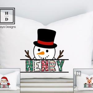 Op de afbeelding: Wit kussen met een sneeuwmanontwerp. De sneeuwman heeft een zwarte hoge hoed met een rode band, takarmen en een wortelneus. De naam "HENRY" staat eronder in kleurrijke, bedrukte letters. Een kerst-thema decoratief kussen.