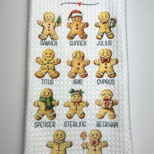 May include: White kitchen towel featuring the text "Grandmom's Favorite Cookies" and illustrations of gingerbread men with names beneath. The gingerbread men are decorated with accessories.