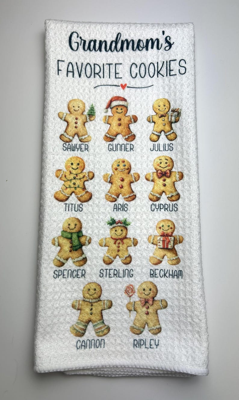 May include: White kitchen towel featuring the text "Grandmom's Favorite Cookies" and illustrations of gingerbread men with names beneath. The gingerbread men are decorated with accessories.