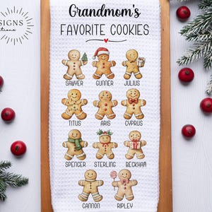 May include: A white kitchen towel with the text "Grandmom's FAVORITE COOKIES" and gingerbread cookie illustrations. The towel is on a wooden board, with red berries and evergreen branches around it.