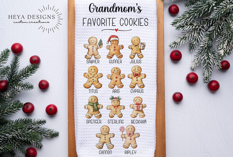 May include: A white kitchen towel with the text "Grandmom's FAVORITE COOKIES" and gingerbread cookie illustrations. The towel is on a wooden board, with red berries and evergreen branches around it.