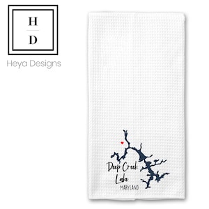 May include: White waffle-weave kitchen towel featuring a navy blue map of Deep Creek Lake, Maryland, with a red heart marking a location. The text "Deep Creek Lake" and "Maryland" are printed below the map. The Heya Designs logo is in the upper left corner.