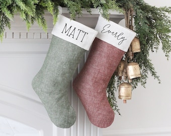 May include: Two personalised Christmas stockings, one green and one red, with white trim and names "Matt" and "Everly" in black lettering.