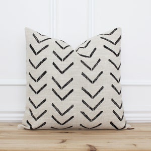 May include: A beige throw pillow with a black chevron pattern. The pillow is made of a soft, textured fabric.
