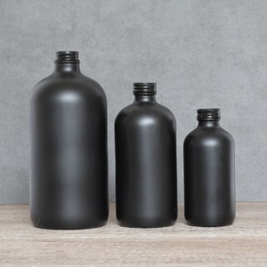 May include: Three black glass bottles of different sizes. The bottles are all opaque and have a smooth, matte finish.