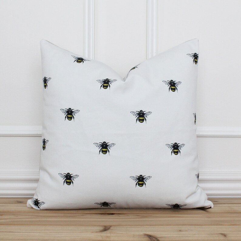 May include: White throw pillow with a repeating pattern of black and yellow bumblebees.