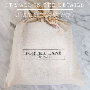 May include: A beige linen pillow cover is packaged in a natural linen drawstring bag with a brown twine tie. The bag has a black label with the text "PORTER LANE home".