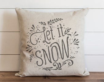 May include: A beige throw pillow with the text "Let it snow" in black script lettering surrounded by a decorative floral design.