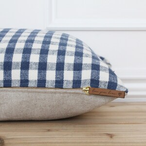 K&ouml;nnte beinhalten: Ein blaues und wei&szlig;es Gingham-Kissen mit Rei&szlig;verschluss und einem braunen Lederanh&auml;nger mit der Aufschrift "Love your home" und einem Herz.