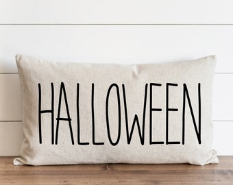 Könnte beinhalten: Ein beiger Kissenbezug mit dem Wort "HALLOWEEN" in Schwarz darauf.