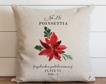 May include: A beige linen pillow with a watercolor illustration of a red poinsettia flower. The pillow has the text "No. 25 POINSETTIA (Euphorbia pulcherrima) PLATE VI VOL. 1" printed on it.