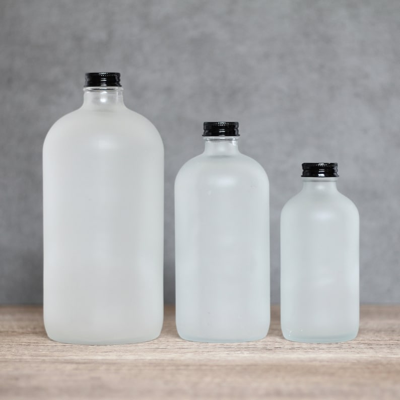 May include: Three frosted glass bottles with black lids. The bottles are different sizes and are arranged from largest to smallest.