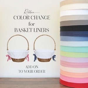 May include: Two wicker baskets with white fabric liners and ribbon handles. The baskets are on a white background with the text "Ribbon Color Change for Basket Liners" and "Add On To Your Order". A stack of ribbon rolls in various colors is on the right side of the image.