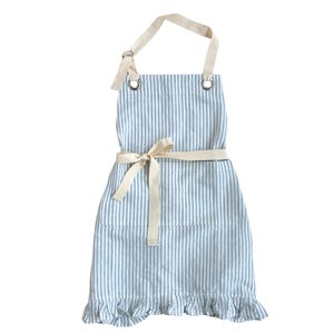 May include: A blue and white striped apron with a cream-colored neck strap and waist tie. The apron has a ruffled hem and metal eyelets for the neck strap. The apron is designed for kitchen use.