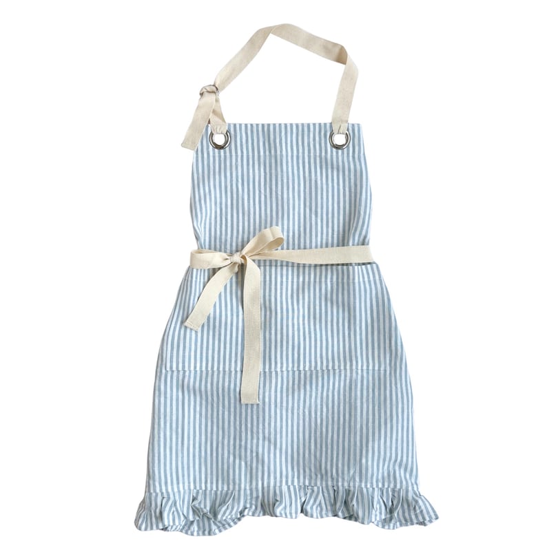 May include: A blue and white striped apron with a cream-colored neck strap and waist tie. The apron has a ruffled hem and metal eyelets for the neck strap. The apron is designed for kitchen use.