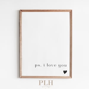 May include: A framed print with a white background and the text "ps. i love you" in black. A small black heart is to the right of the text. The frame is made of light brown wood.