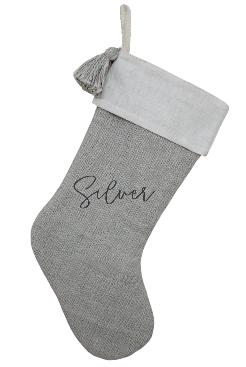 May include: A gray Christmas stocking with a white cuff and a matching tassel. The word "Silver" is written in cursive on the front. The stocking has a loop for hanging.