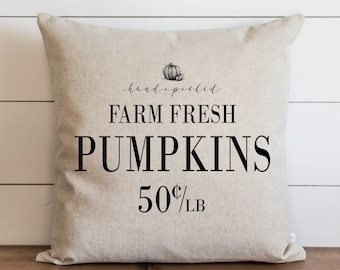 May include: A beige pillow with black text that reads "hand-picked FARM FRESH PUMPKINS 50¢/LB". A small black and white illustration of two pumpkins is above the text.