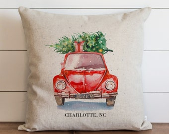 May include: A red vintage car with a Christmas tree and a gift on top, driving through a snowy scene. The car has a license plate that says "LUCKY" and the text "CHARLOTTE, NC" is printed below the car.