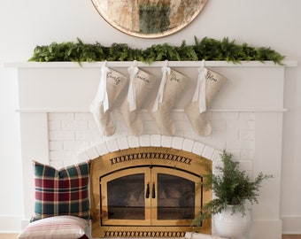 May include: A white brick fireplace with a gold metal fire screen. There are four stockings hung on the mantel with the names "Everly", "ander", "Ded", and "Mon" written on them.