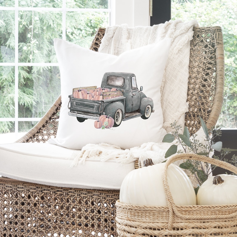 May include: A white throw pillow with a watercolor illustration of a vintage pickup truck filled with pink pumpkins. The truck is driving on a white background.